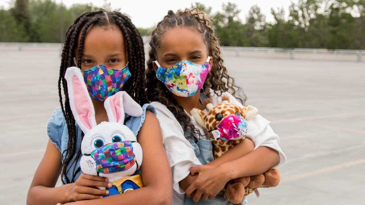 two young girls with stuffies wearing matching face masks