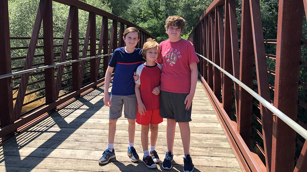 Three kids posing for a picture on a walking bridge in a park
