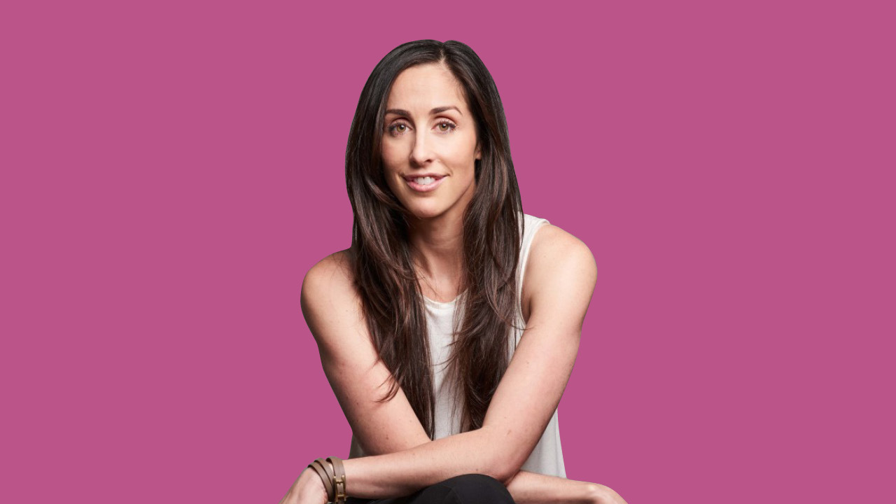 Catherine Reitman sitting in front of a pink background