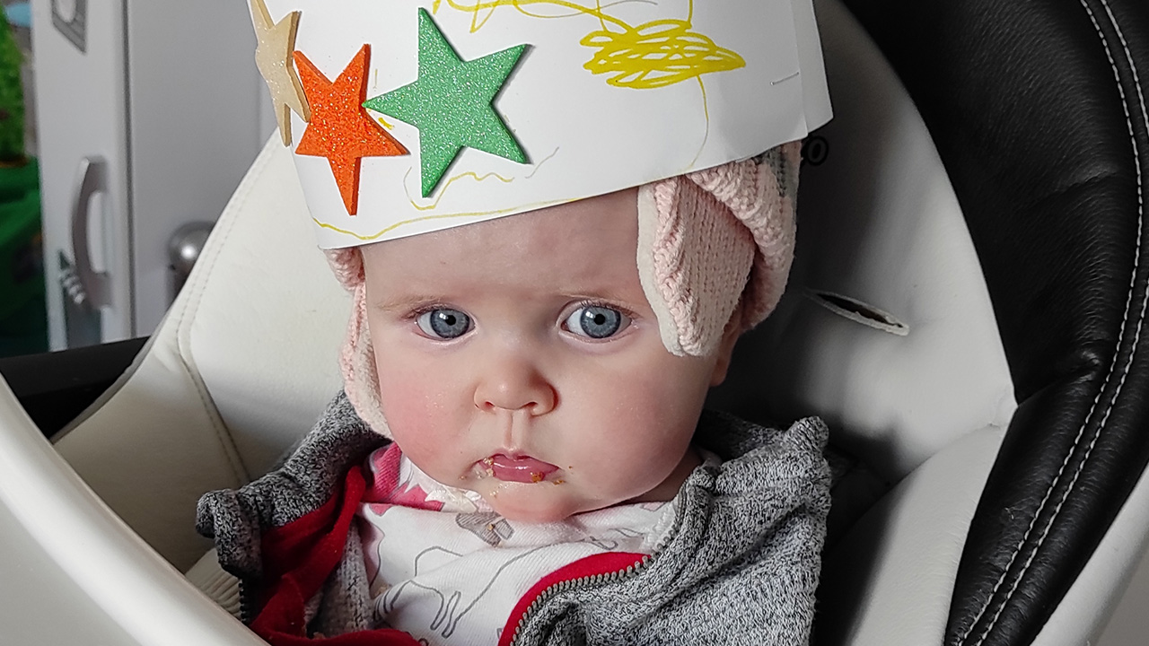 a baby in their high chair wearing a paper crown with stars on it